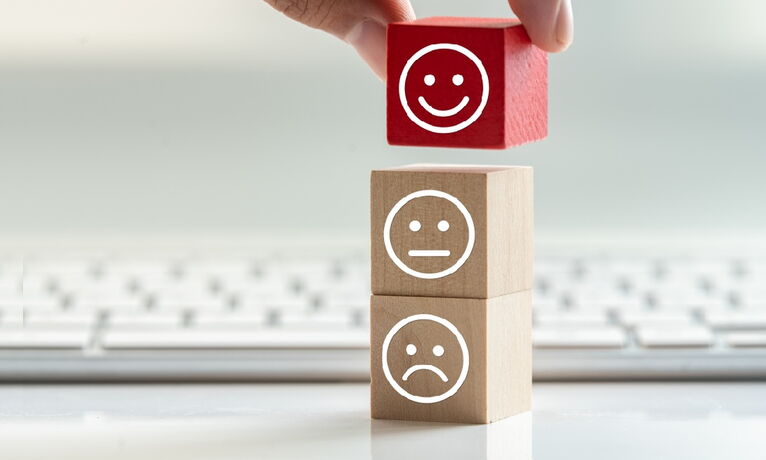 Une main place un dé rouge avec un visage souriant sur deux autres dés qui affichent des visages neutres et tristes.